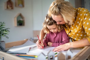 A cute small girl with mother in bedroom indoors at home, drawing pictures.