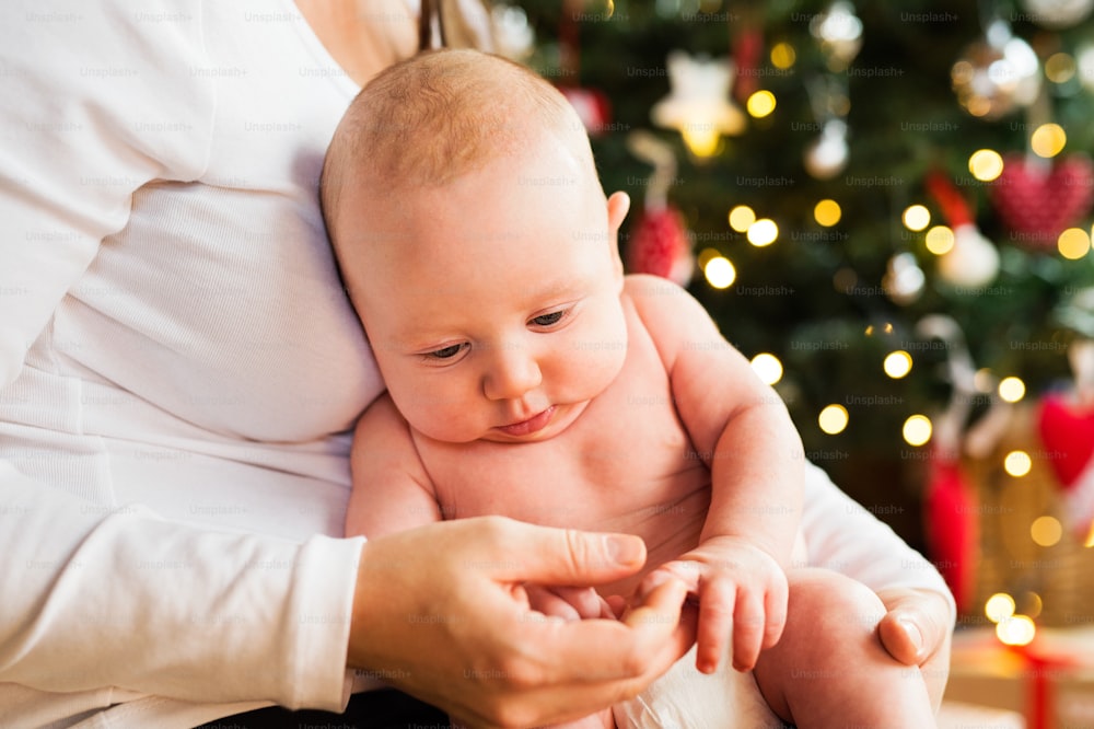 Unrecognizable woman holding a naked baby boy in her arms at Christmas time.