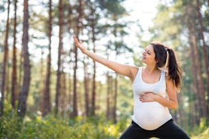 Retrato da vista frontal da mulher grávida feliz ao ar livre na natureza, fazendo exercício.