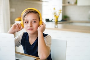 A small boy with headphones and laptop sitting at the table indoors at home.