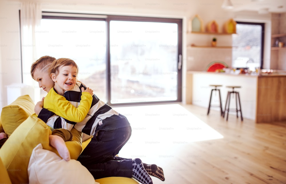 Side view of two happy children sitting on sofa indoors at home, hugging.