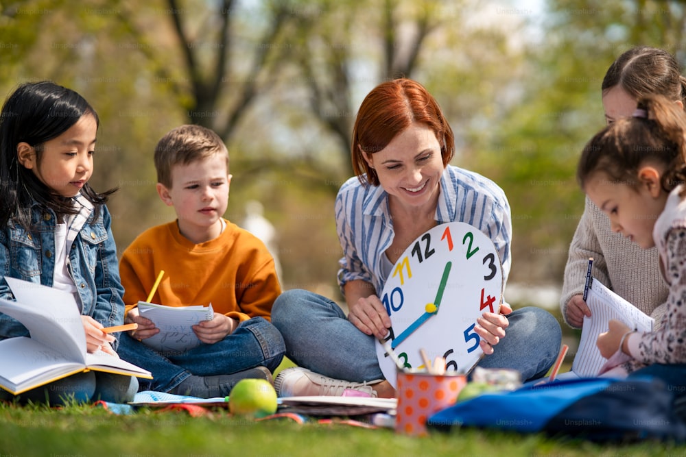 Ein Lehrer mit kleinen Kindern sitzt draußen im Stadtpark, Lerngruppen-Bildungskonzept.