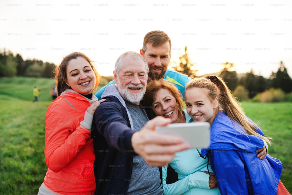 Un gruppo di persone in forma e attive che riposano dopo aver fatto esercizio nella natura, scattando selfie con lo smartphone.