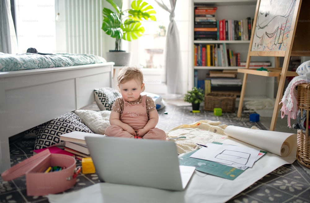 집 바닥에 있는 작은 유아 소녀가 노트북으로 이야기 이야기를 보고 있다.