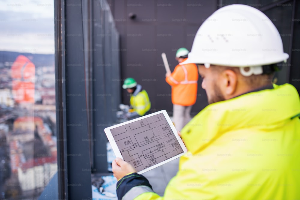 Ingeniero hombre maduro de pie en el sitio de construcción, sosteniendo una tableta con planos.
