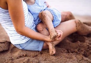 A midsection of breasfeeding toddler daughter on beach on summer holiday.