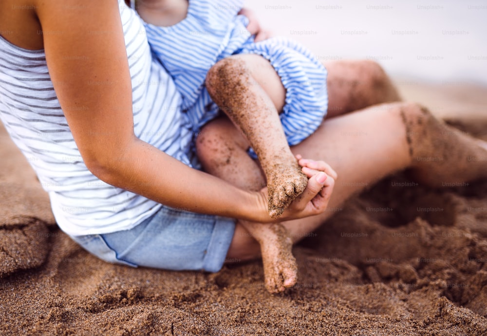 A midsection of breasfeeding toddler daughter on beach on summer holiday.