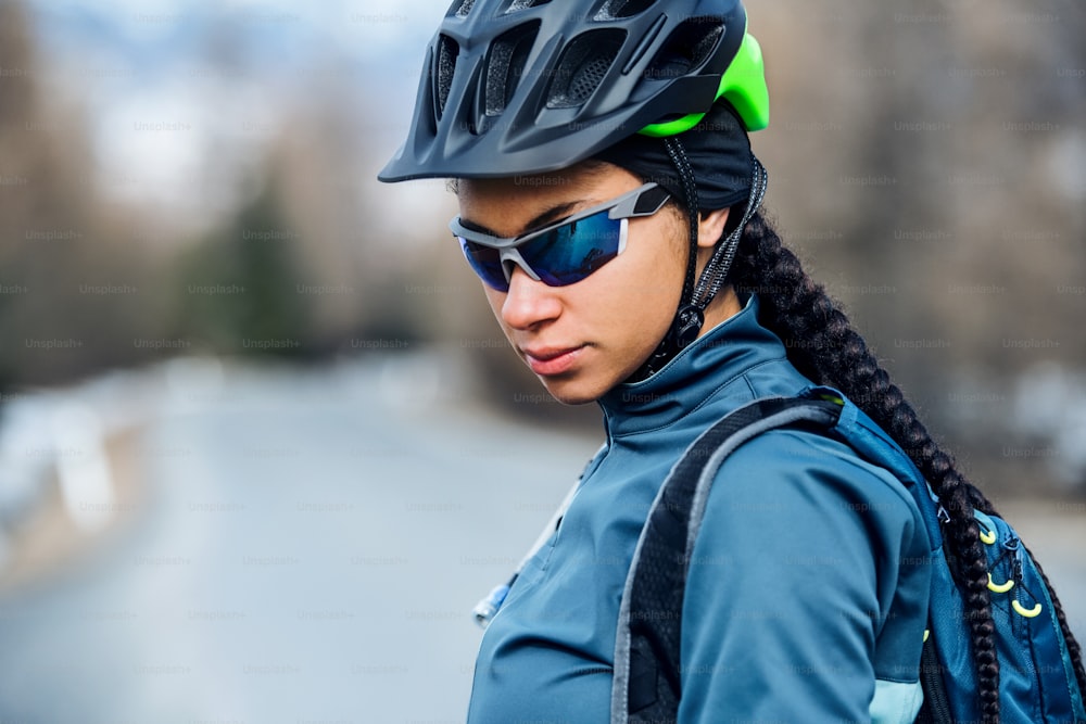 Ciclista de montanha fêmea com óculos de sol em pé na estrada ao ar livre no inverno.