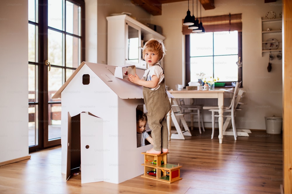 Deux enfants en bas âge jouant avec une maison en papier en carton à l’intérieur à la maison. Espace de copie.