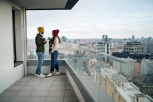 Felici proprietari di giovani coppie con caffè sul balcone in un nuovo appartamento, in movimento, in una nuova casa e in un concetto di trasferimento.