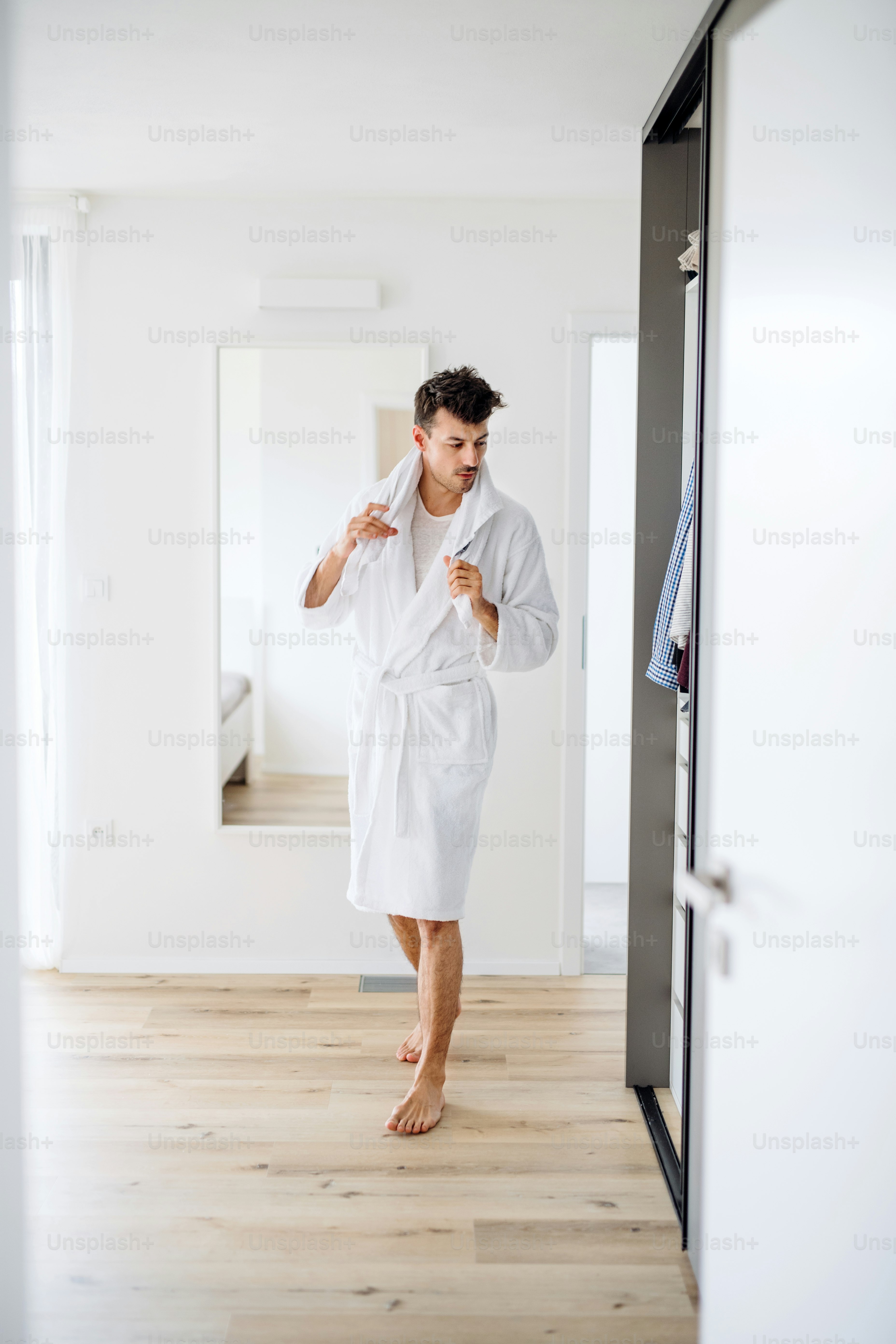 Junger Mann mit Bademantel geht im Schlafzimmer, eine Morgenroutine.