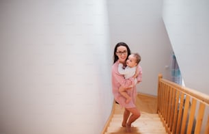 A young mother carrying small toddler son down the stairs indoors at home, looking back.