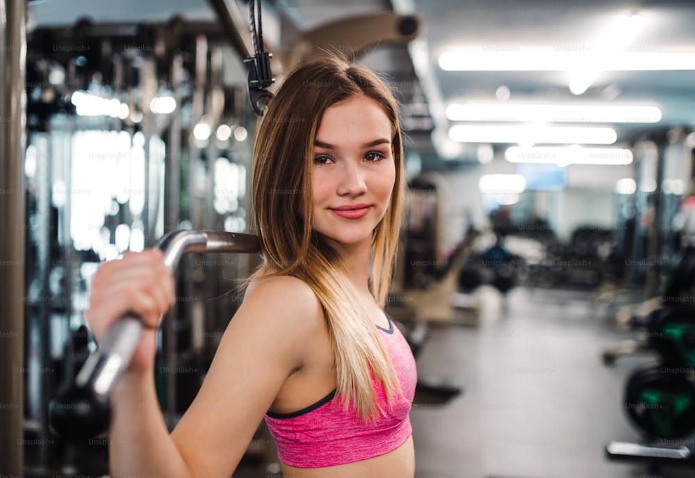 A side view of a beautiful young girl or woman doing strength workout in a gym.