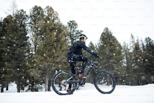 A side view of mountain biker riding in snow outdoors in winter nature.