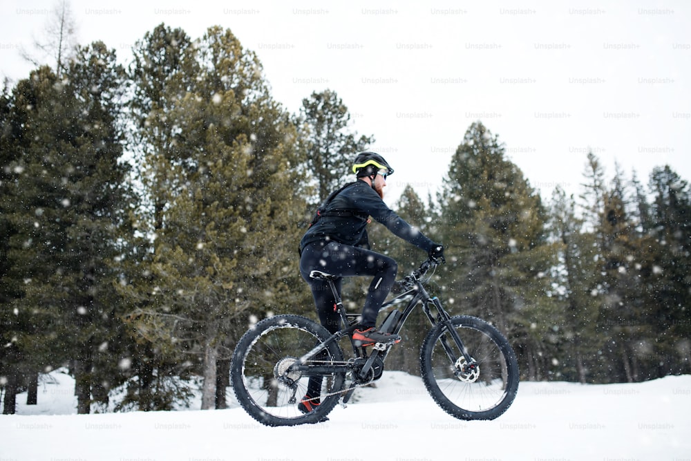 Una vista laterale del mountain biker che cavalca sulla neve all'aperto nella natura invernale.
