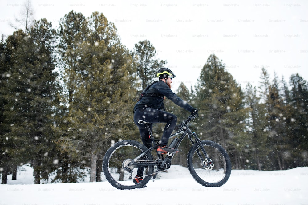 A side view of mountain biker riding in snow outdoors in winter nature.