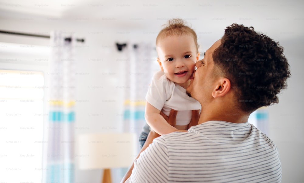 A portrait of cheerful father and small toddler son indoors at home, kissing.