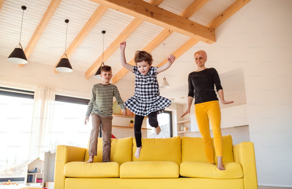 Une jeune femme avec deux enfants sautant sur un canapé à la maison, en train de s’amuser.