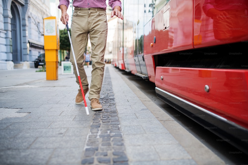 Una sección media de un hombre ciego mayor con bastón blanco subiendo al transporte público en la ciudad.