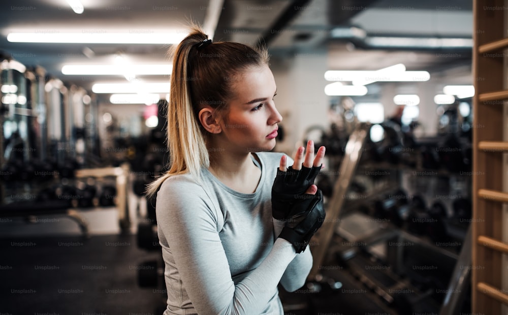 Menina ou mulher com luvas sem dedos, fazendo treino em uma academia.