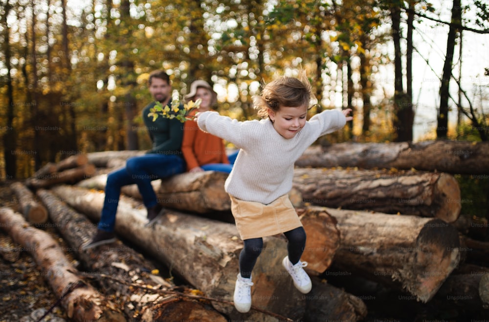 Happy small girl with parents on a walk in autumn forest, jumping.