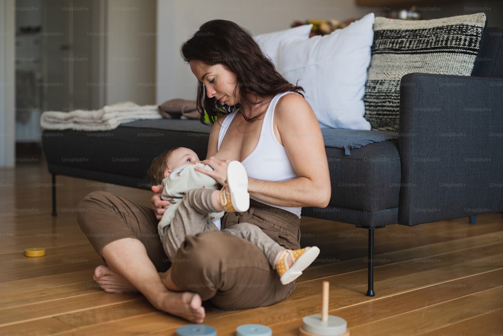 Madre joven feliz amamantando al bebé pequeño en el interior de casa, concepto de lactancia materna.