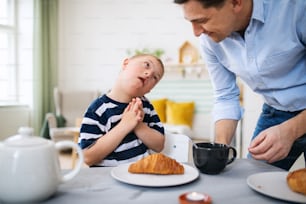 A down syndrome boy with father at the table, having breakfast.
