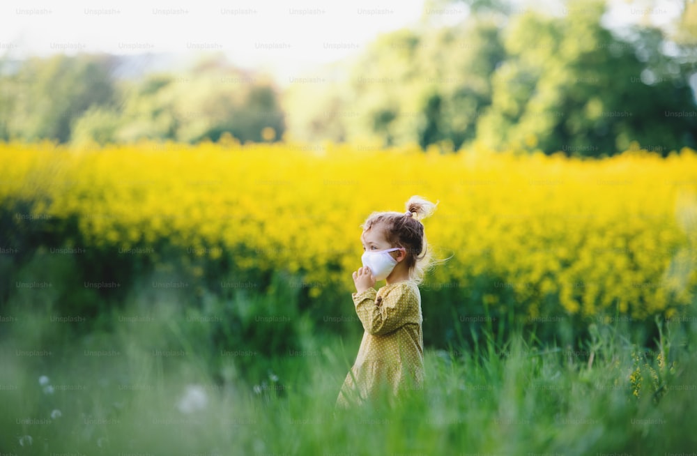 Side view of happy small toddler girl standing in spring nature in rapeseed field.