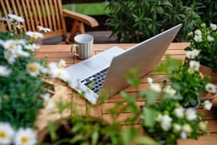 Draufsicht auf Laptop und Kaffee auf Tisch auf Balkon im Sommer, Bürokonzept im Freien.