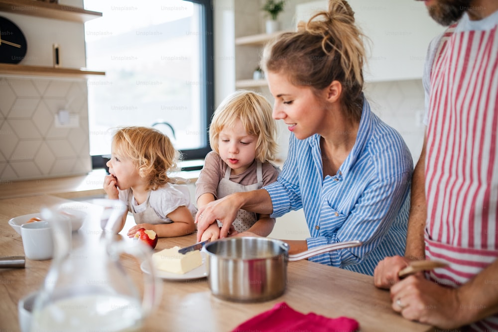Eine junge Familie mit zwei kleinen Kindern drinnen in der Küche und bereitet Essen zu.