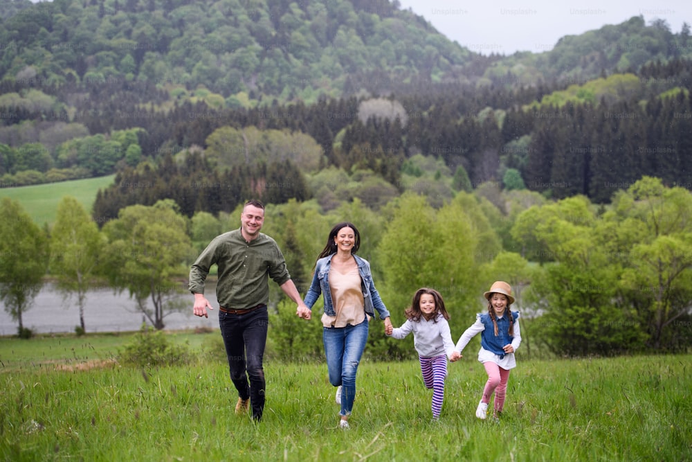 Família feliz com duas filhas pequenas correndo ao ar livre na natureza da primavera, de mãos dadas.