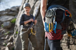 Un instructor irreconocible con arnés y mosquetones escalando rocas con personas mayores al aire libre en la naturaleza, estilo de vida activo.
