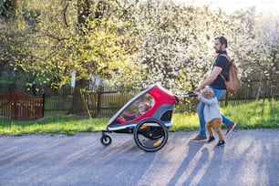 A father with toddler son pushing a jogging stroller outside. A walk in spring nature.
