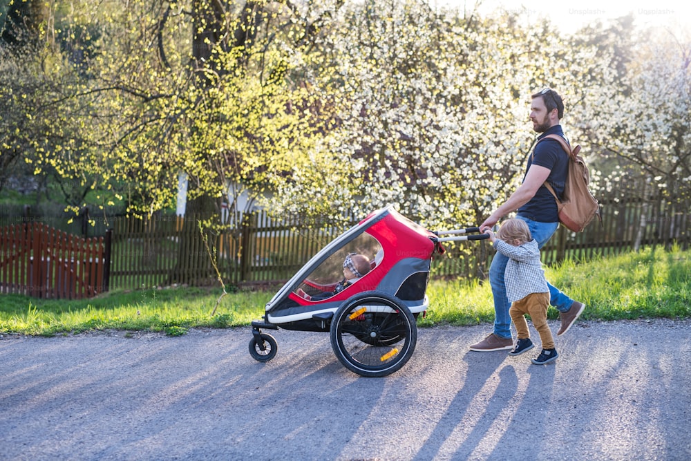 A father with toddler son pushing a jogging stroller outside. A walk in spring nature.