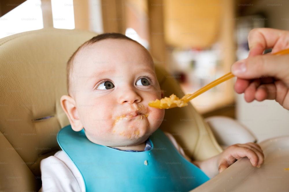 スプーンを使って赤ん坊の息子に餌をやる見分けがつかない母親。