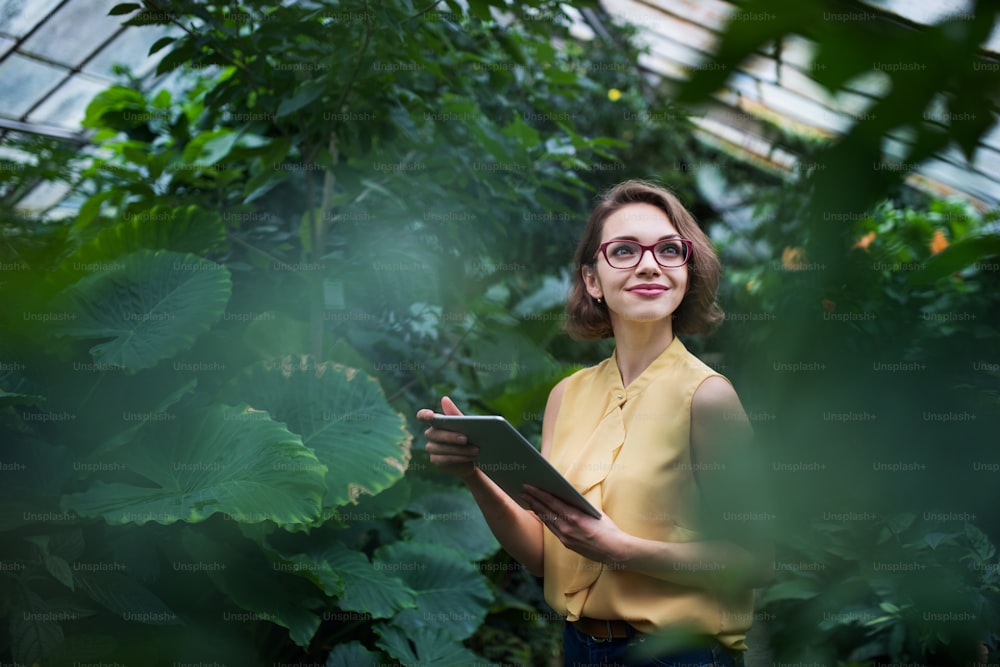 Mujer joven con tableta de pie en invernadero en jardín botánico. Espacio de copia.