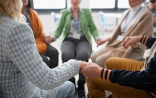 Eine Gruppe älterer Menschen, die während der Therapiesitzung im Kreis sitzen, Händchen halten und gemeinsam beten.