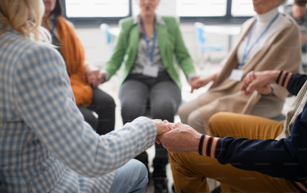 A group of senior people sitting in circle during therapy session, holding hands and praying together.