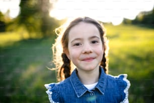 Front view portrait of small girl standing outdoors in spring nature, looking at camera.