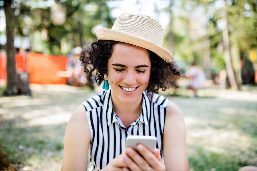 Vista frontale della giovane donna al festival estivo o alla vacanza in campeggio, utilizzando lo smartphone.