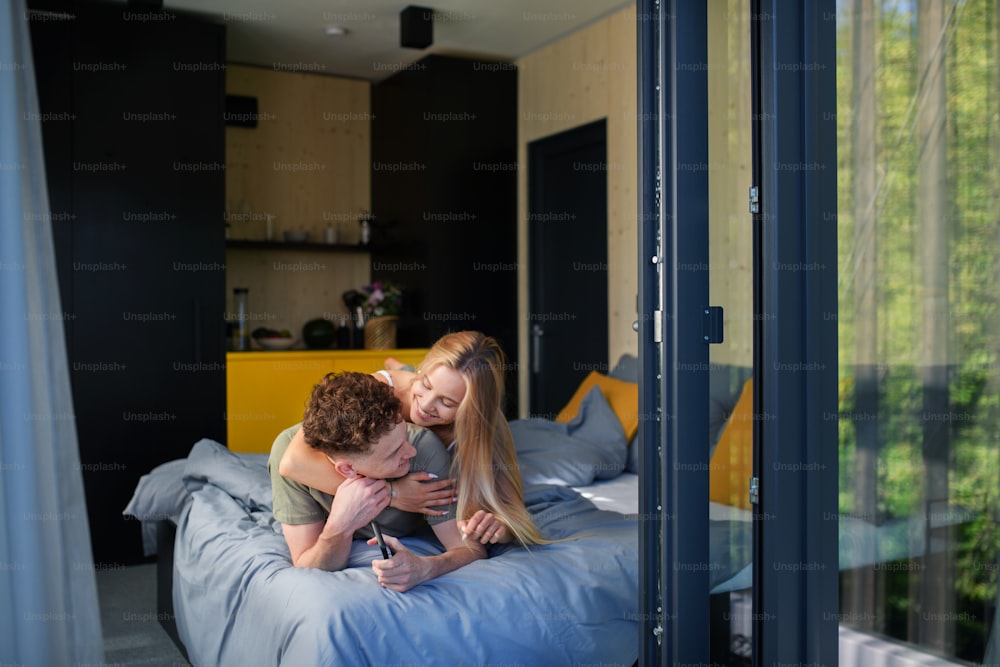 Um jovem casal feliz no amor deitado na cama de manhã em sua nova casa em casa minúscula, conceito de vida sustentável.
