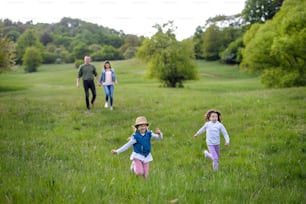 Glückliche Familie mit zwei kleinen Töchtern, die im Frühling in der Natur im Freien laufen und Spaß haben.