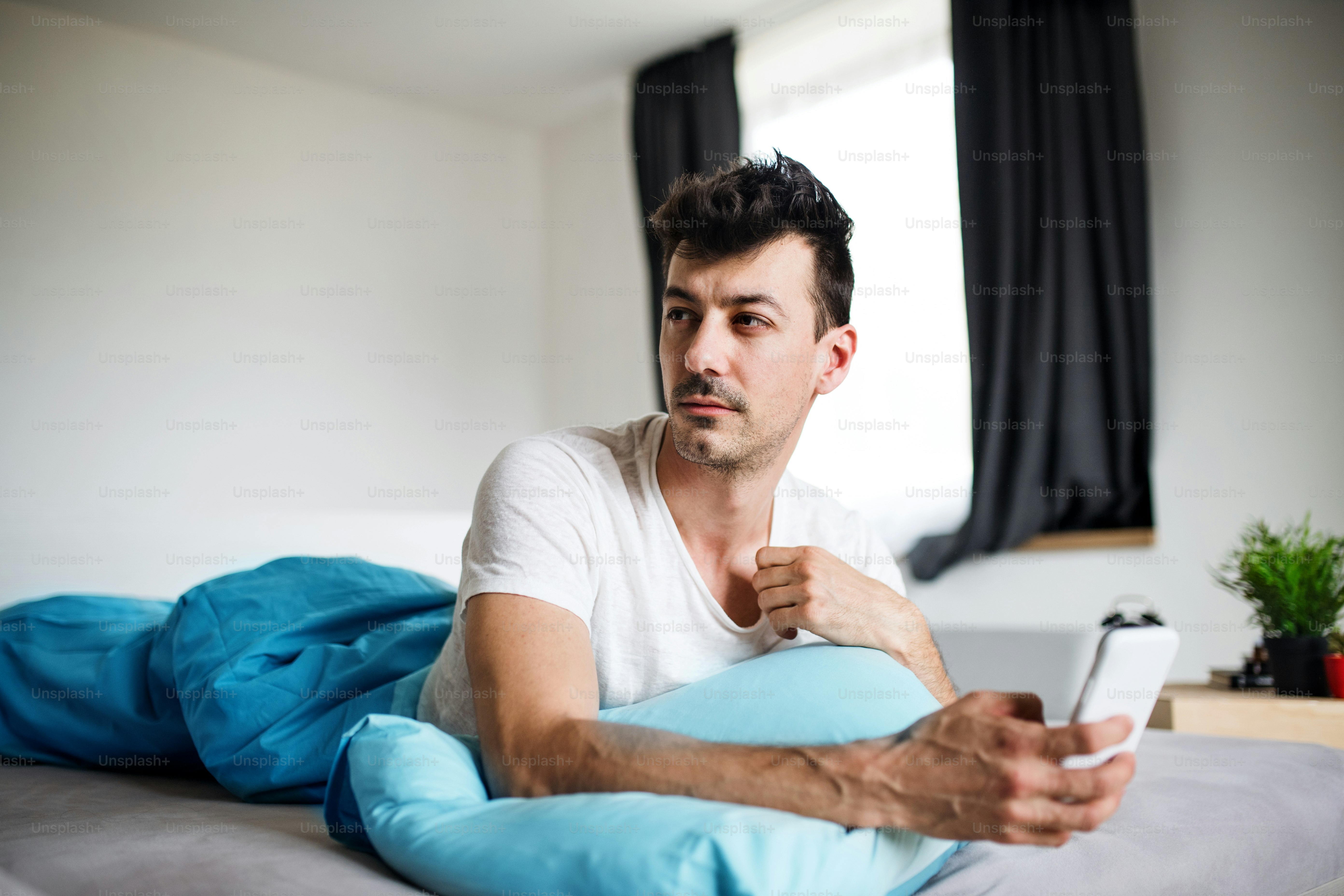 Ein junger Mann mit Smartphone im Bett zu Hause, SMS.