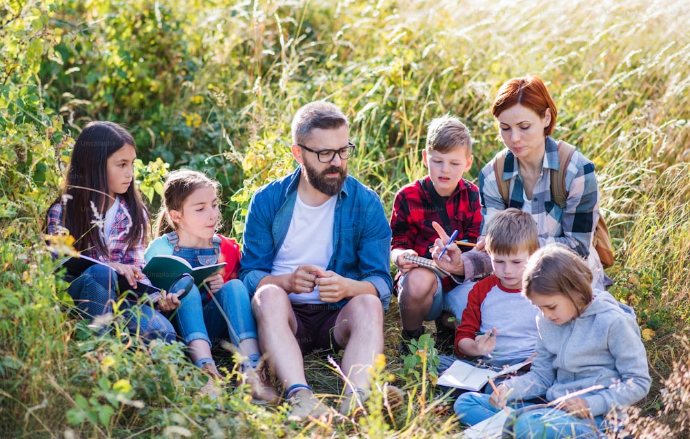 Un gruppo di piccoli scolari con insegnante in gita nella natura, imparando.