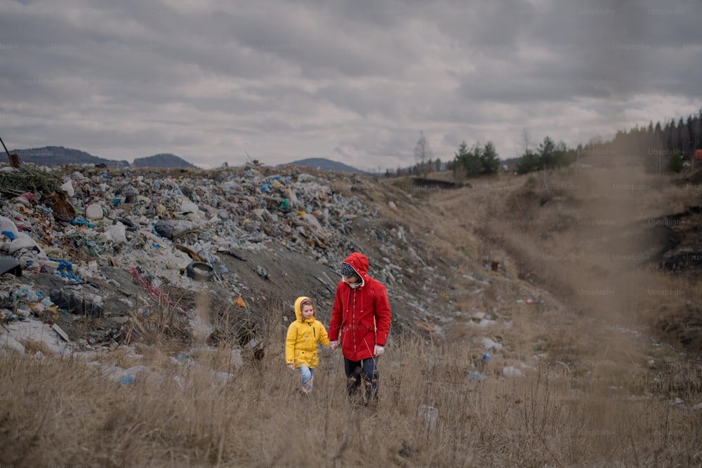 Vorderansicht eines Vaters mit kleiner Tochter Aktivistin geht auf Mülldeponie, Umweltkonzept.