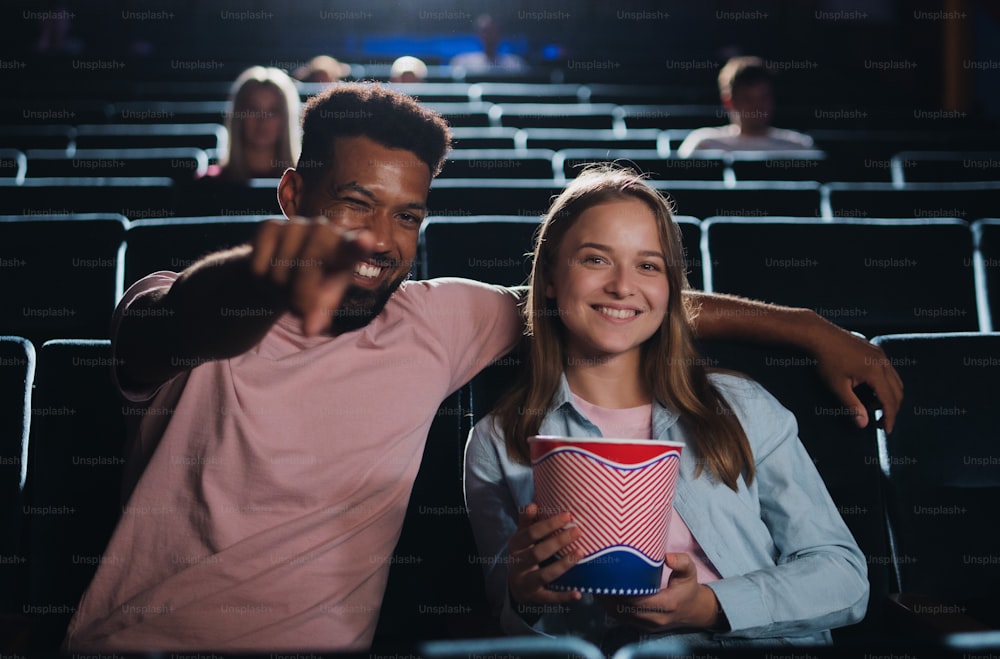 Una vista frontal de una pareja joven y alegre en el cine, apuntando a la cámara.