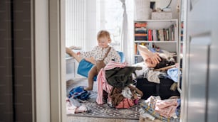 Tired and frustrated mother with small toddler daughter in messy bedroom at home, resting.