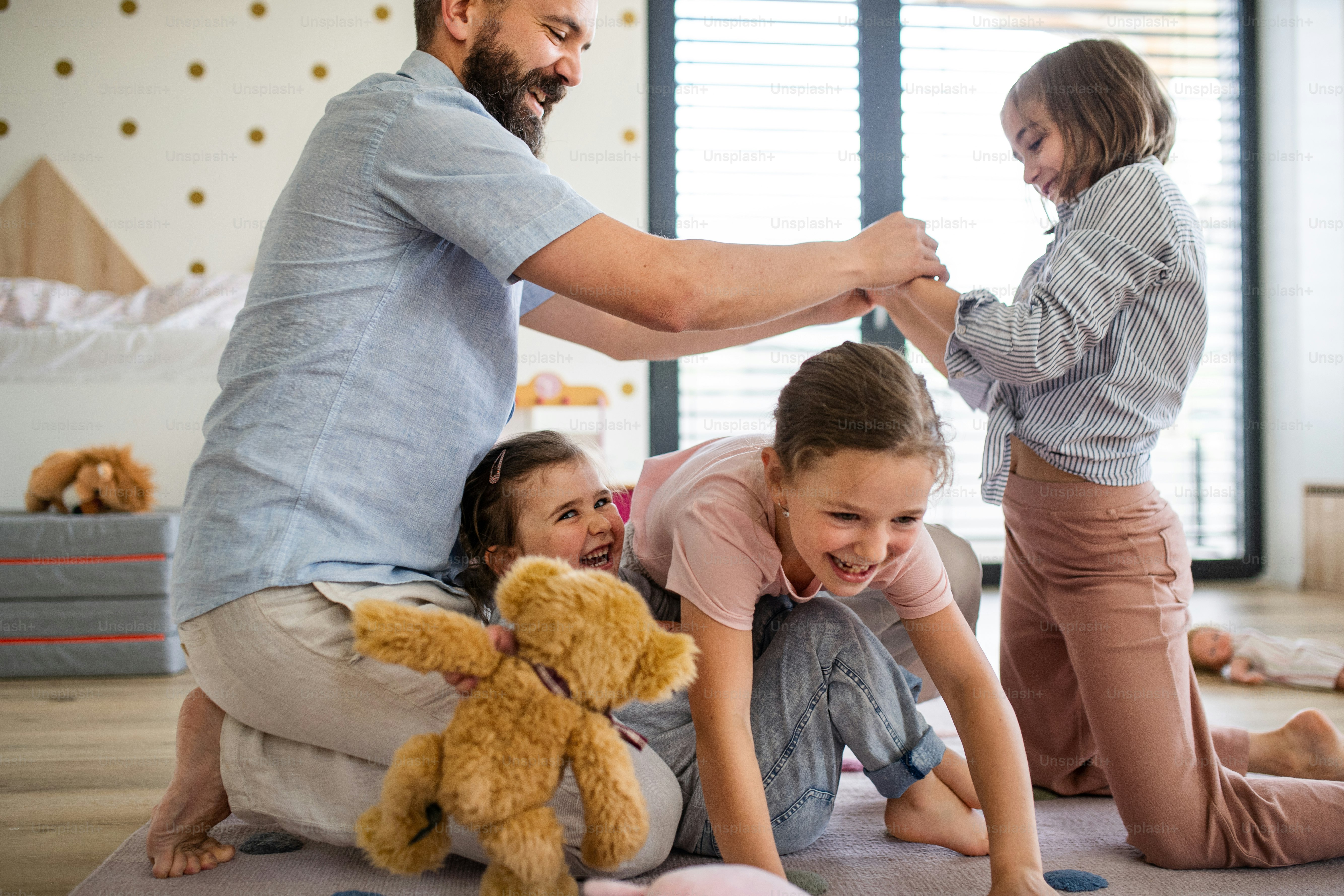 A father with three daughters indoors at home, playing on floor