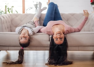 Portrait of mother with small daughter on sofa indoors at home, looking at camera upside down.