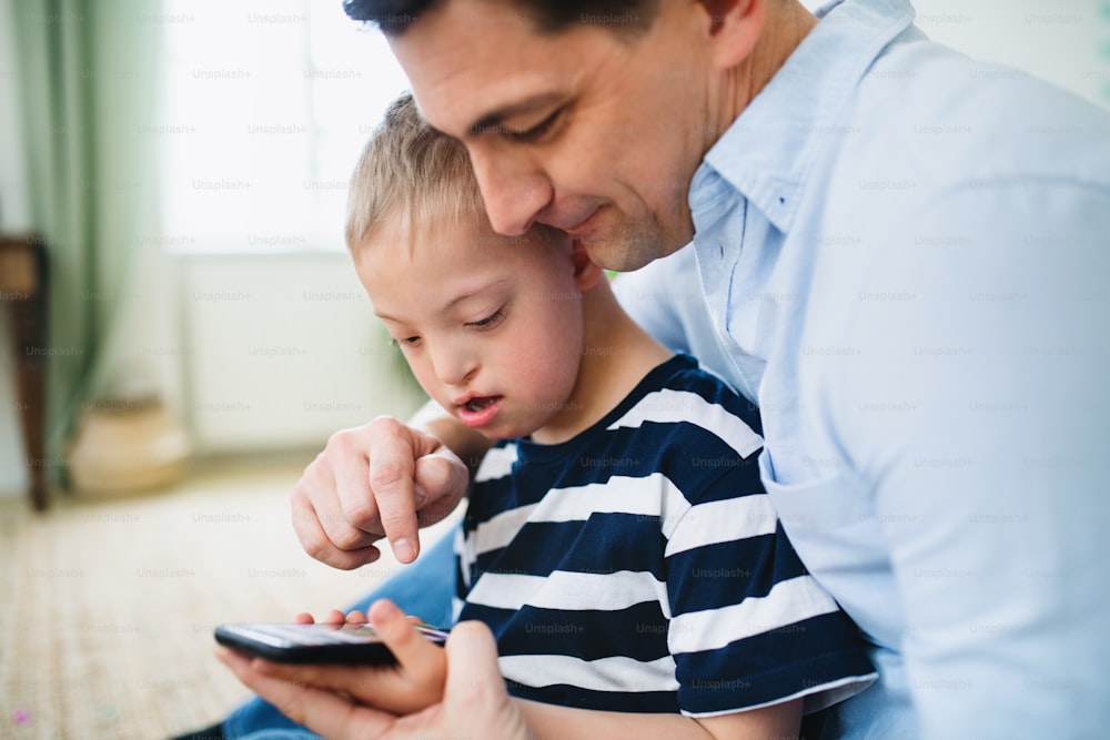 Um pai com síndrome de down feliz filho dentro de casa em casa, usando smartphone.